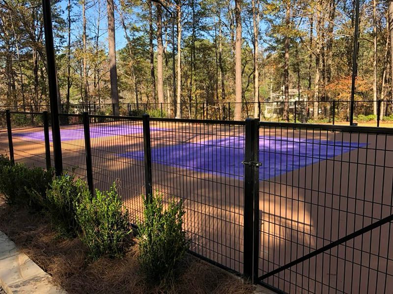 A fence surrounds a basketball court in the middle of a forest.