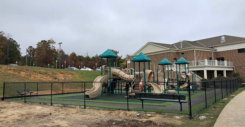 A playground with a fence around it and a brick building in the background.