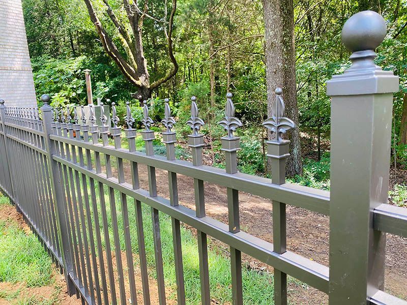 A close up of a wrought iron fence with trees in the background.