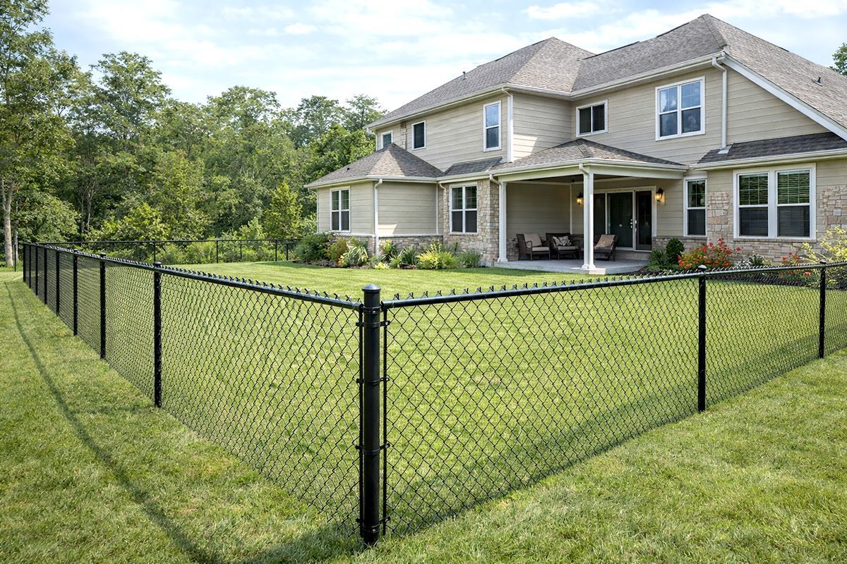 A black chain-link fence surrounds a lush green lawn in front of a tan suburban house with a patio.
