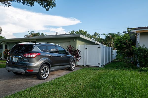 A car is parked in front of a house with a white fence.