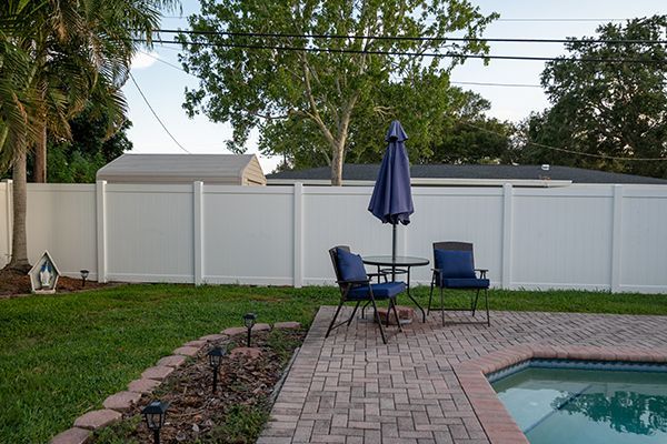 A patio with a table and chairs and an umbrella next to a pool.