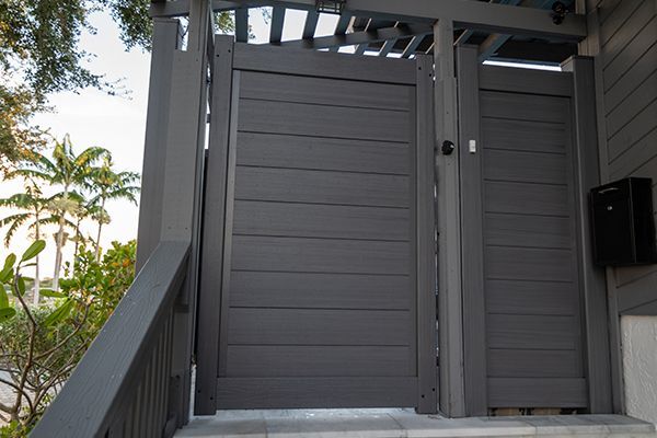 A gray gate is sitting on top of a staircase next to a house.