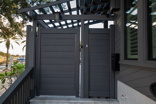 A black gate is leading to a house with a pergola.