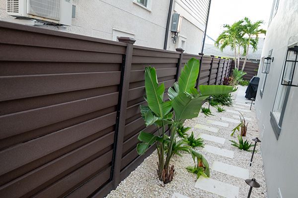 A wooden fence surrounds a garden with plants and gravel.