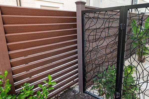 A wooden fence with a black gate in front of it.
