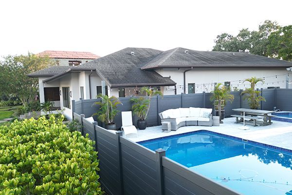 A fence surrounds a large swimming pool in front of a house.