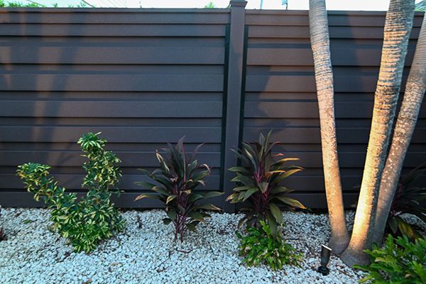 A fence with plants and rocks in front of it.