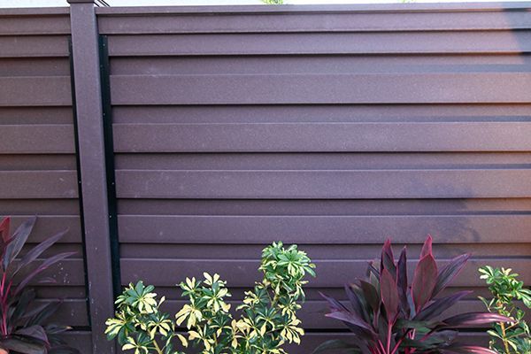 A wooden fence with plants in front of it.