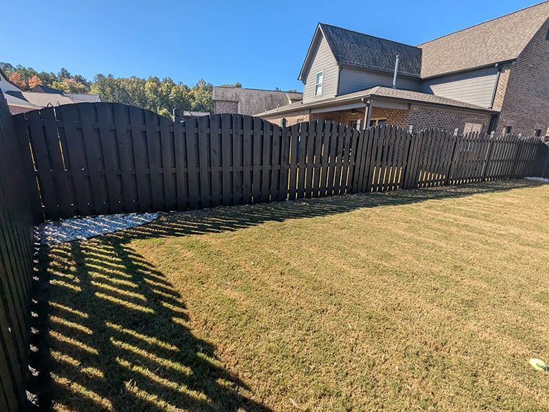 A wooden fence surrounds a lush green yard in front of a house.