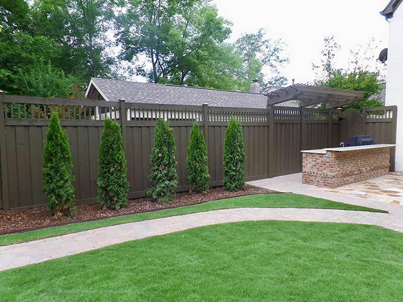 A wooden fence surrounds a lush green lawn in a backyard.