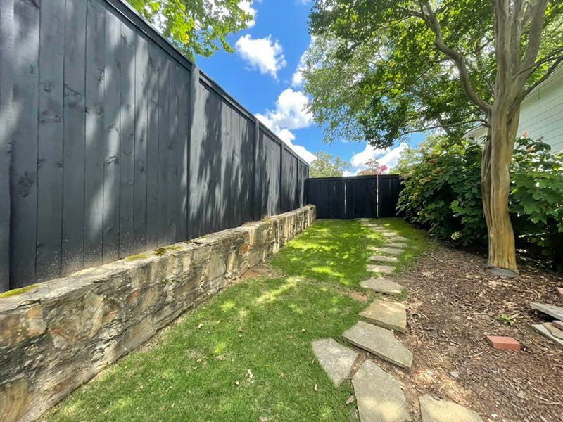 A stone path leading to a black fence in a backyard.