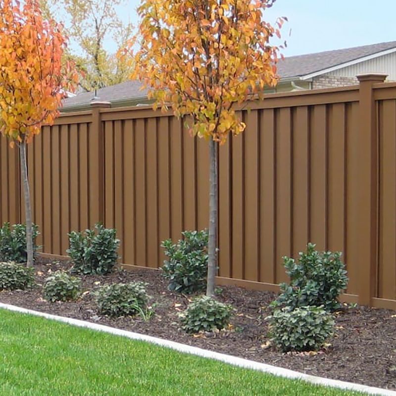 A brown wooden fence surrounds a lush green yard with trees and bushes.