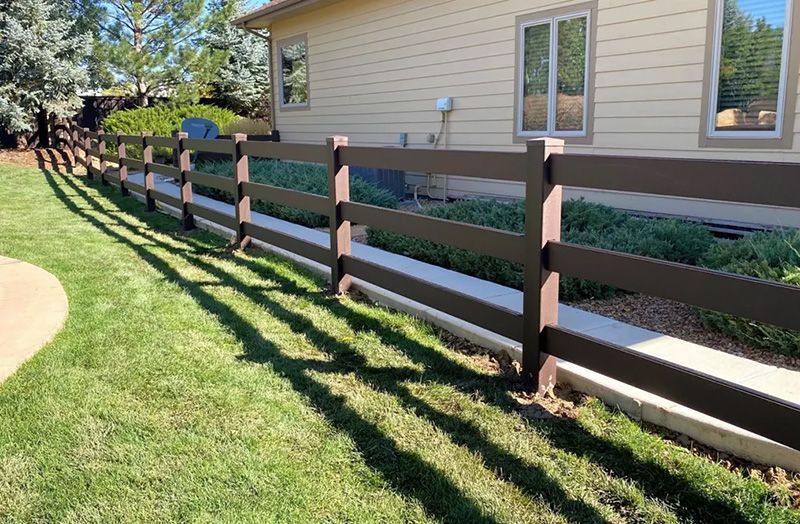 A wooden fence surrounds a lush green yard in front of a house.