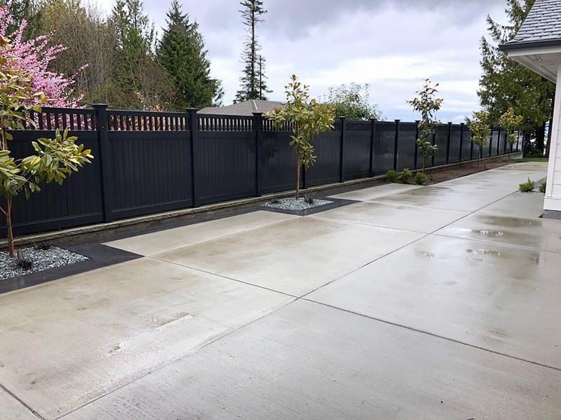 A black fence surrounds a concrete driveway in front of a house.