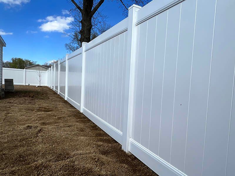 A white vinyl fence is in the backyard of a house.