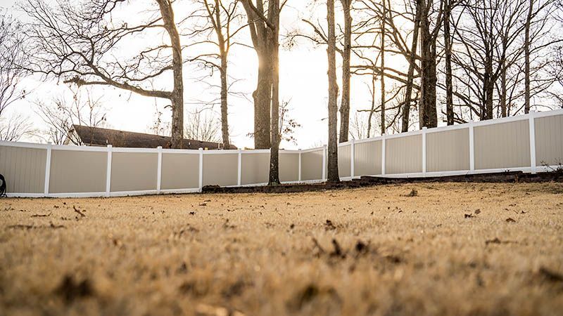 A white fence surrounds a yard with trees in the background.