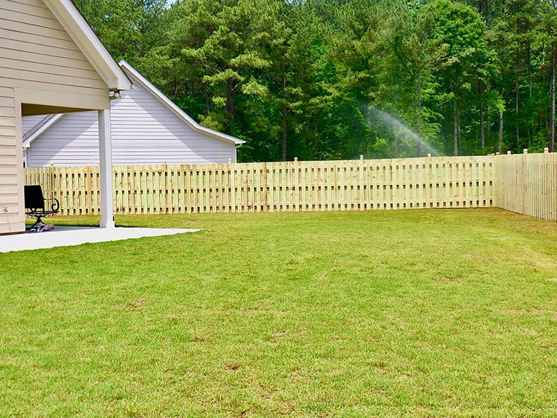 A backyard with a wooden fence and a house in the background.