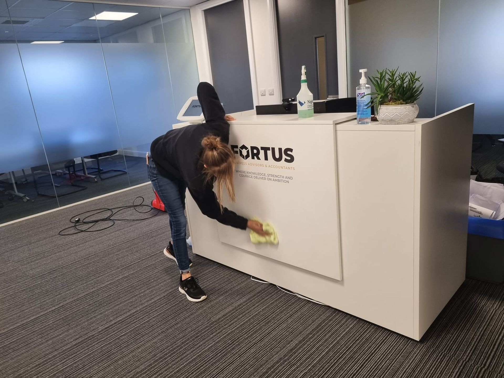 A woman is cleaning a reception desk in an office.