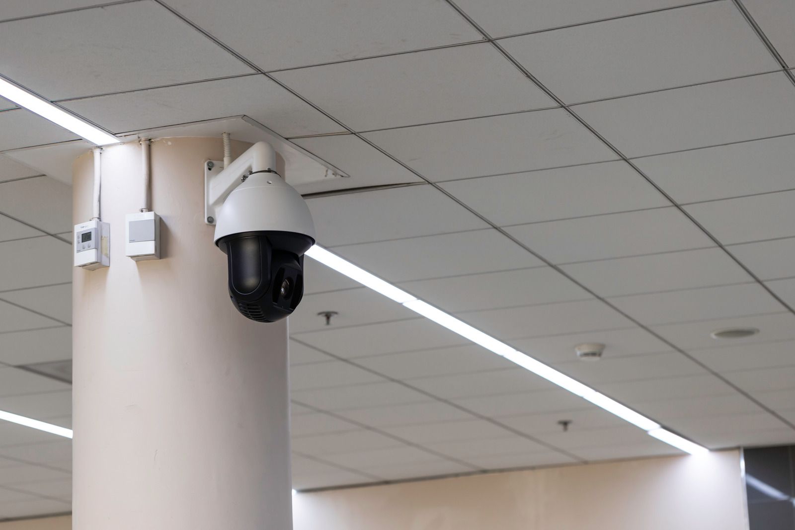 Security camera mounted on a pillar, with boxes and wiring. Ceiling lights in background.