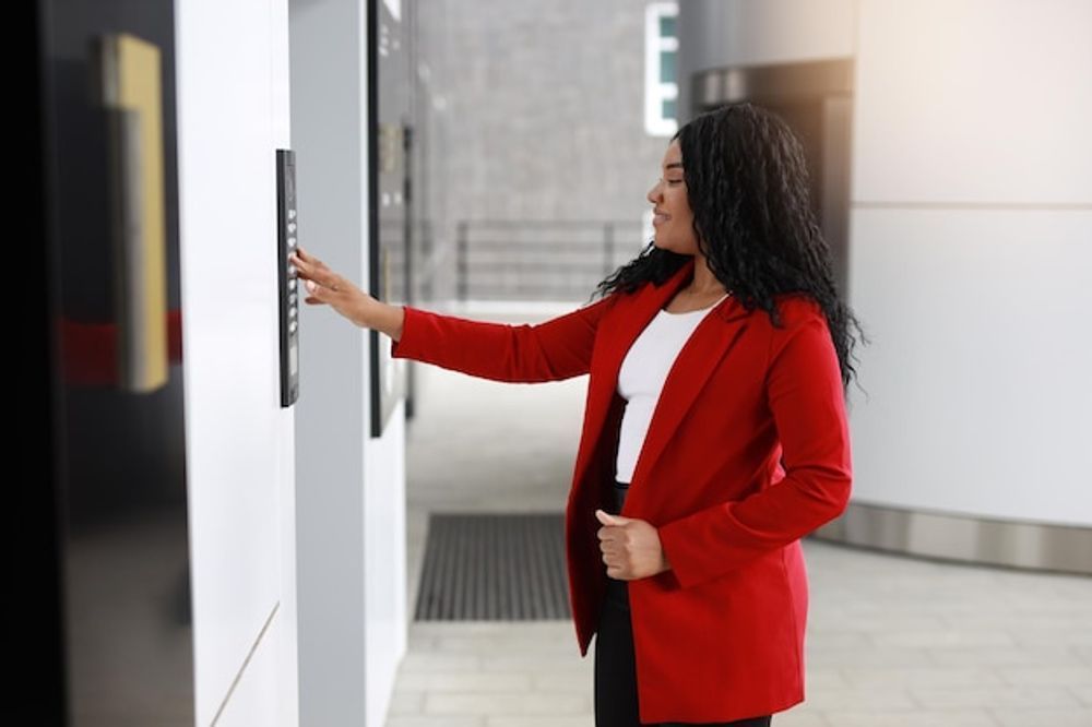 Woman in red blazer presses elevator button in a modern building.