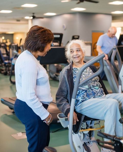 Caregiver in blue scrubs assists an older person using a walker in a home setting.