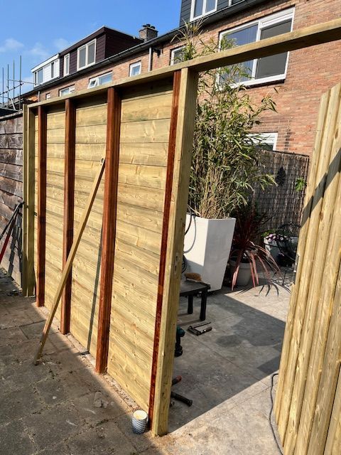 Een houten schutting in aanbouw. ​​Bruine palen en horizontale planken zijn bevestigd aan verticale steunen. Zonnige achtertuin.