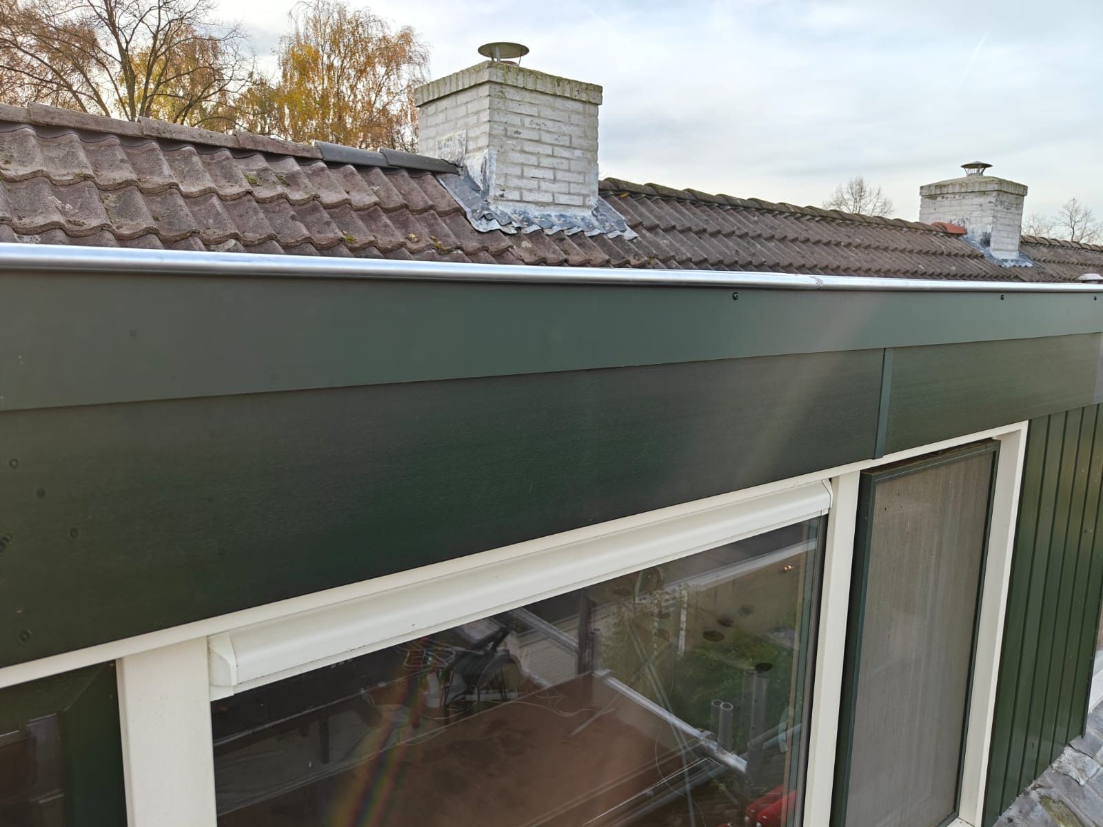 Groen gebouw met een pannendak, schoorstenen en een raam; bewolkte lucht.