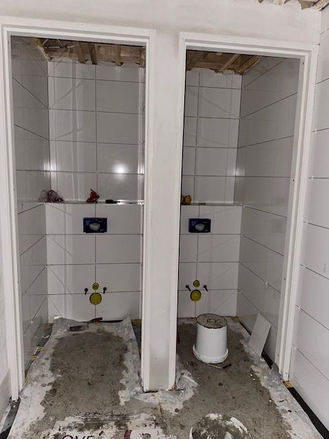 Twee naast elkaar gelegen stallen met witte betegelde muren, toiletten en open deuren; er is bouwafval zichtbaar.