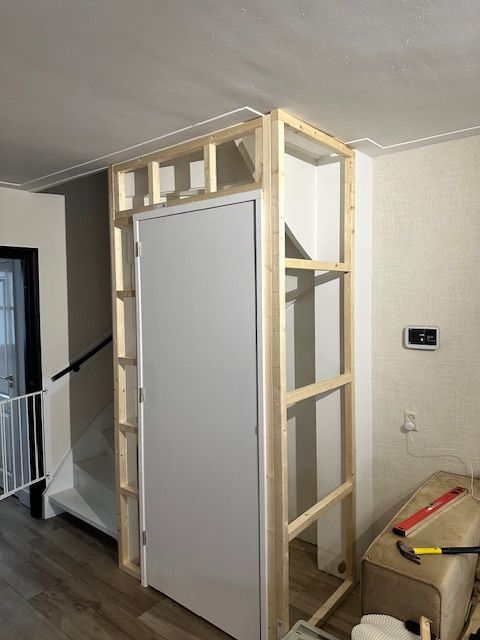 Houten frame rond een witte deur, waarschijnlijk een kast, in een gang. De constructie is nog niet af.