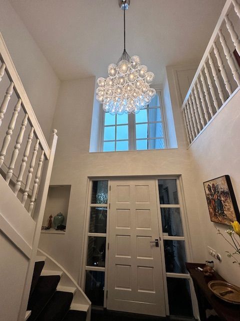 Entree met een kroonluchter, witte trap en een raam boven de voordeur.