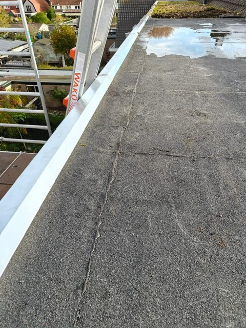 Plat dak met waterplassen, aluminium lood en een ladder.