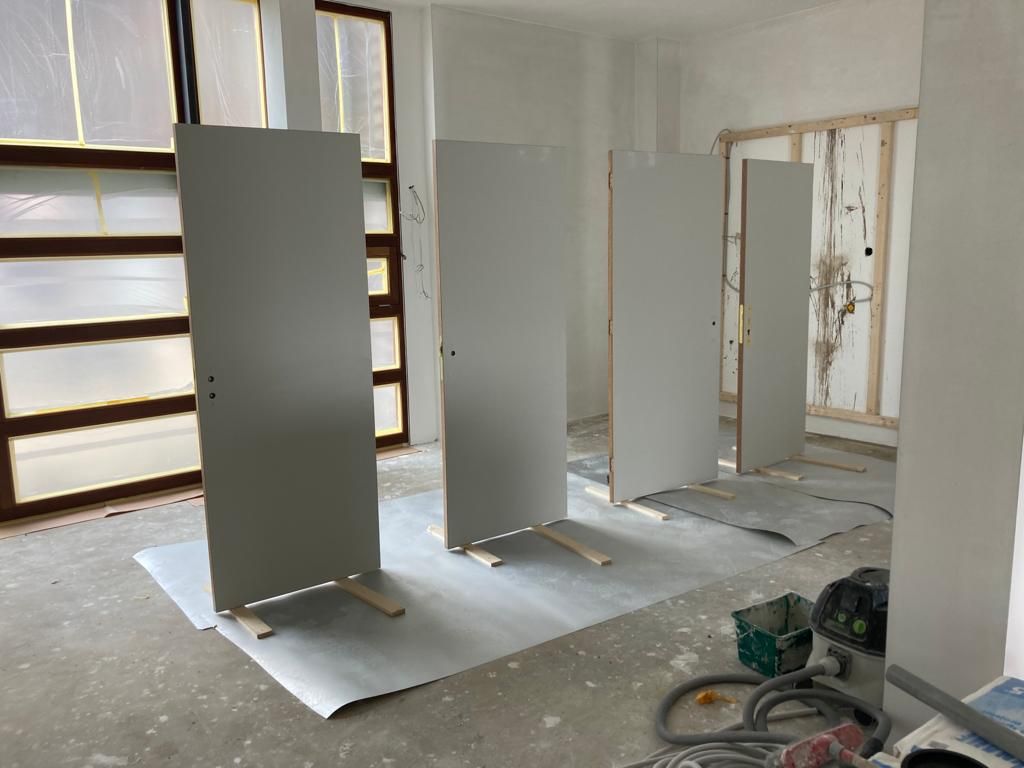 Vier grijze deuren staan ​​tegen een muur in een kamer in aanbouw, met gereedschap en materialen in de buurt.