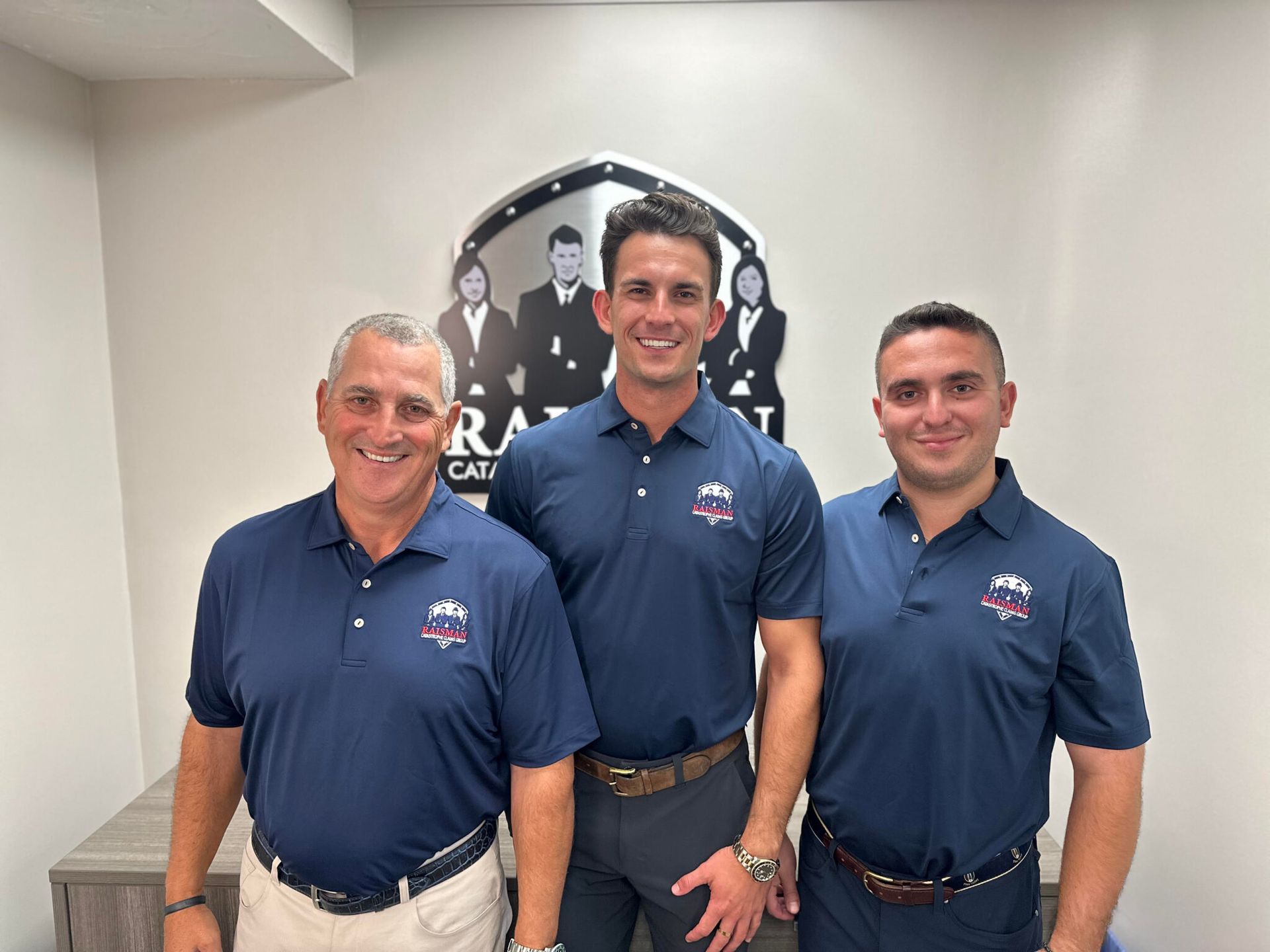 Three men in blue shirts are standing next to each other in a room.