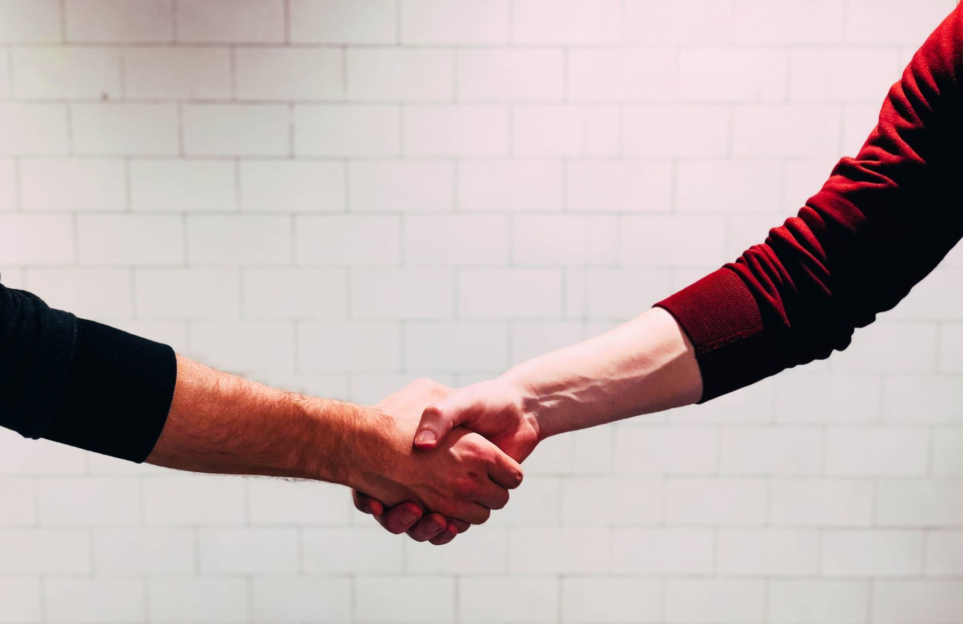 Two people are shaking hands in front of a white brick wall.