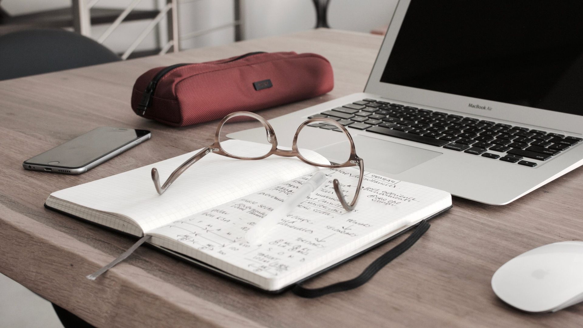 A pair of glasses is sitting on top of a notebook next to a laptop.