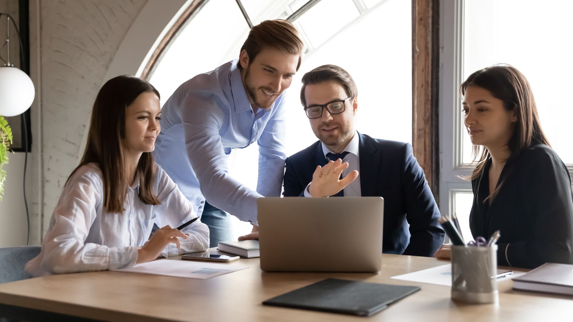 A group of people are sitting around a table looking at a laptop computer.