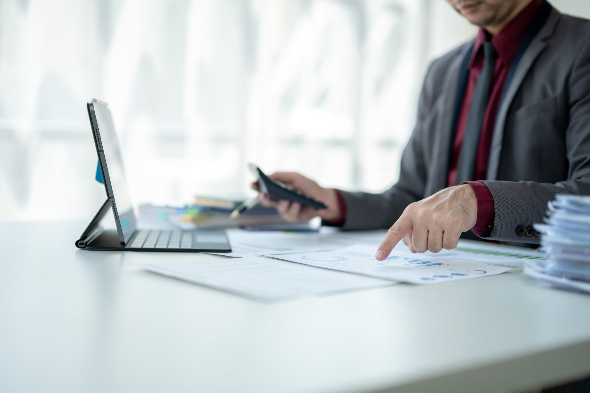 A man is sitting at a desk using a tablet and a cell phone.