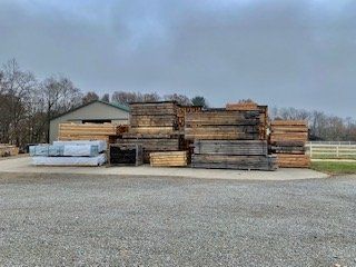 A pile of wood is sitting in a gravel lot in front of a building.