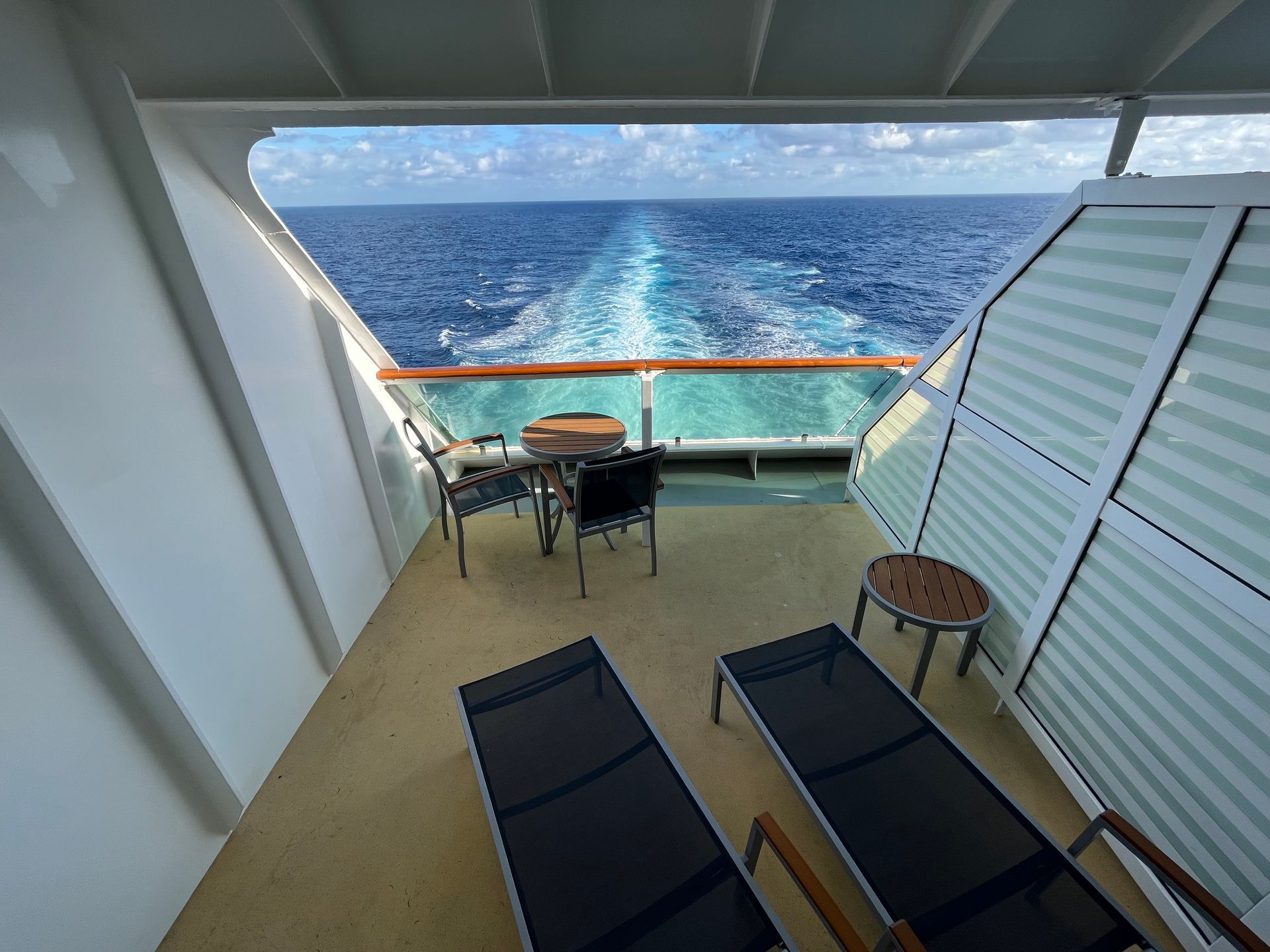 Balcony of a cruise ship with ocean view, chairs, and chaise lounges.