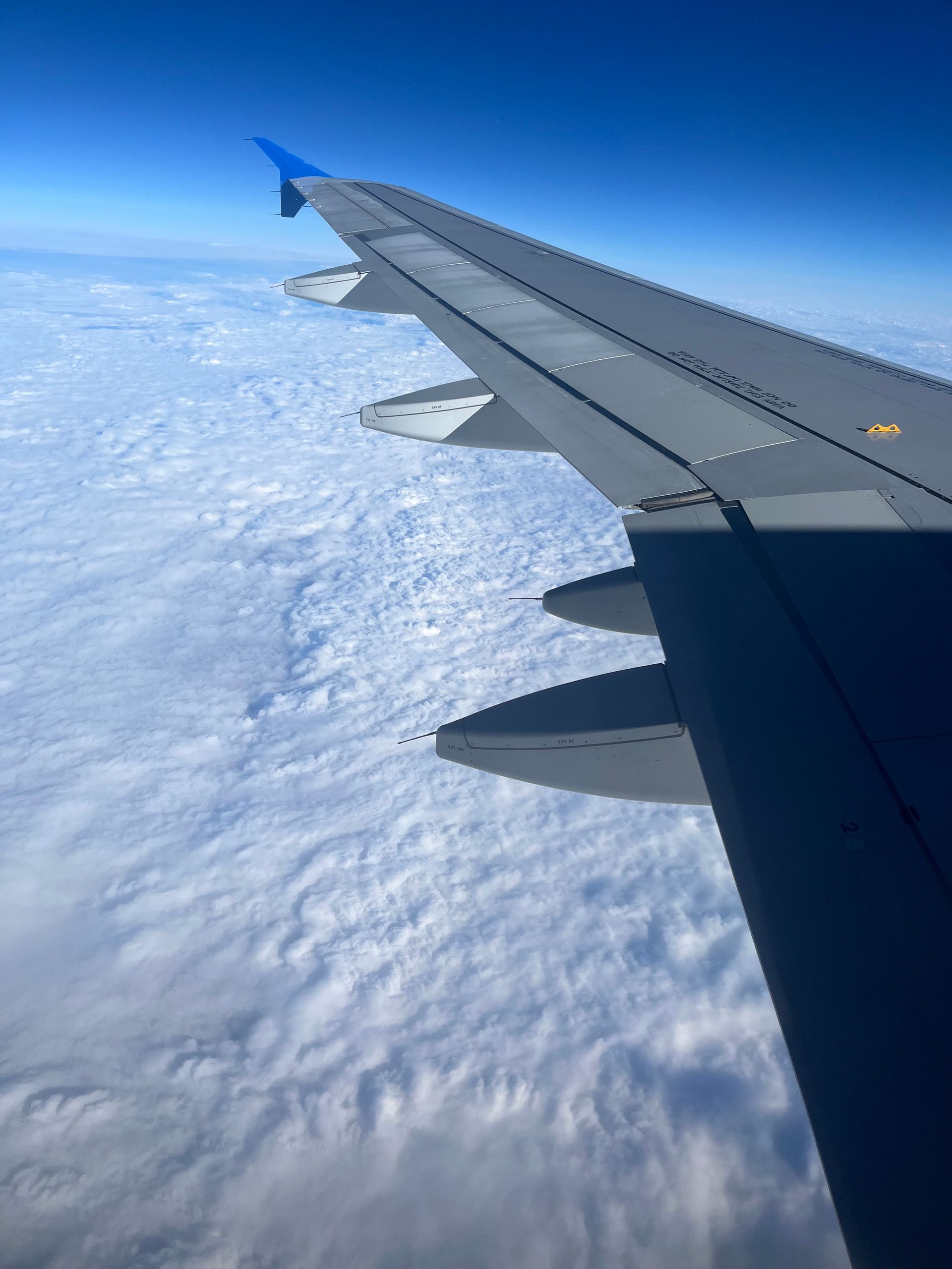 Airplane wing against a backdrop of clouds and blue sky.