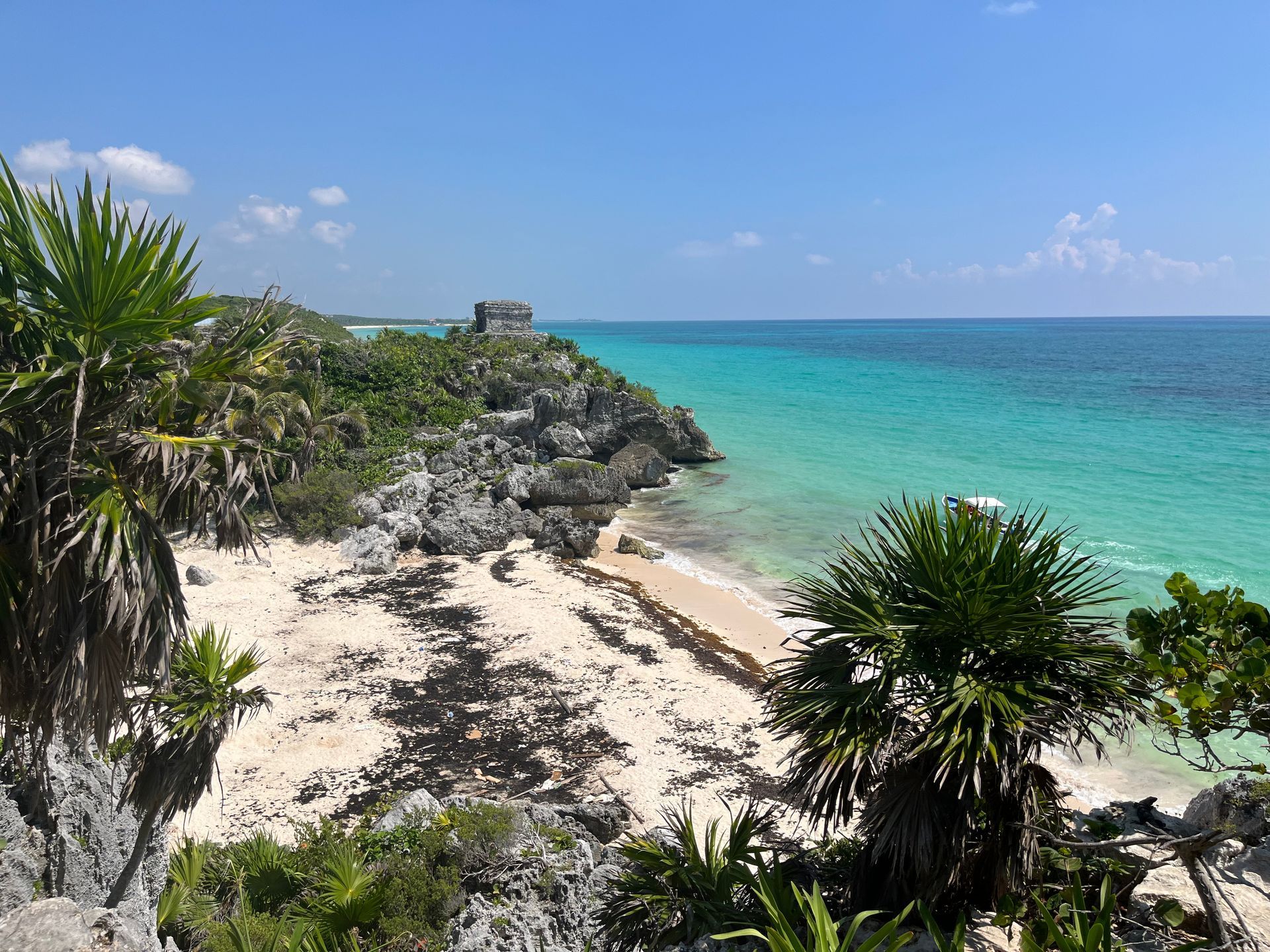 Rocky coastline with white sand beach and turquoise water under a blue sky.