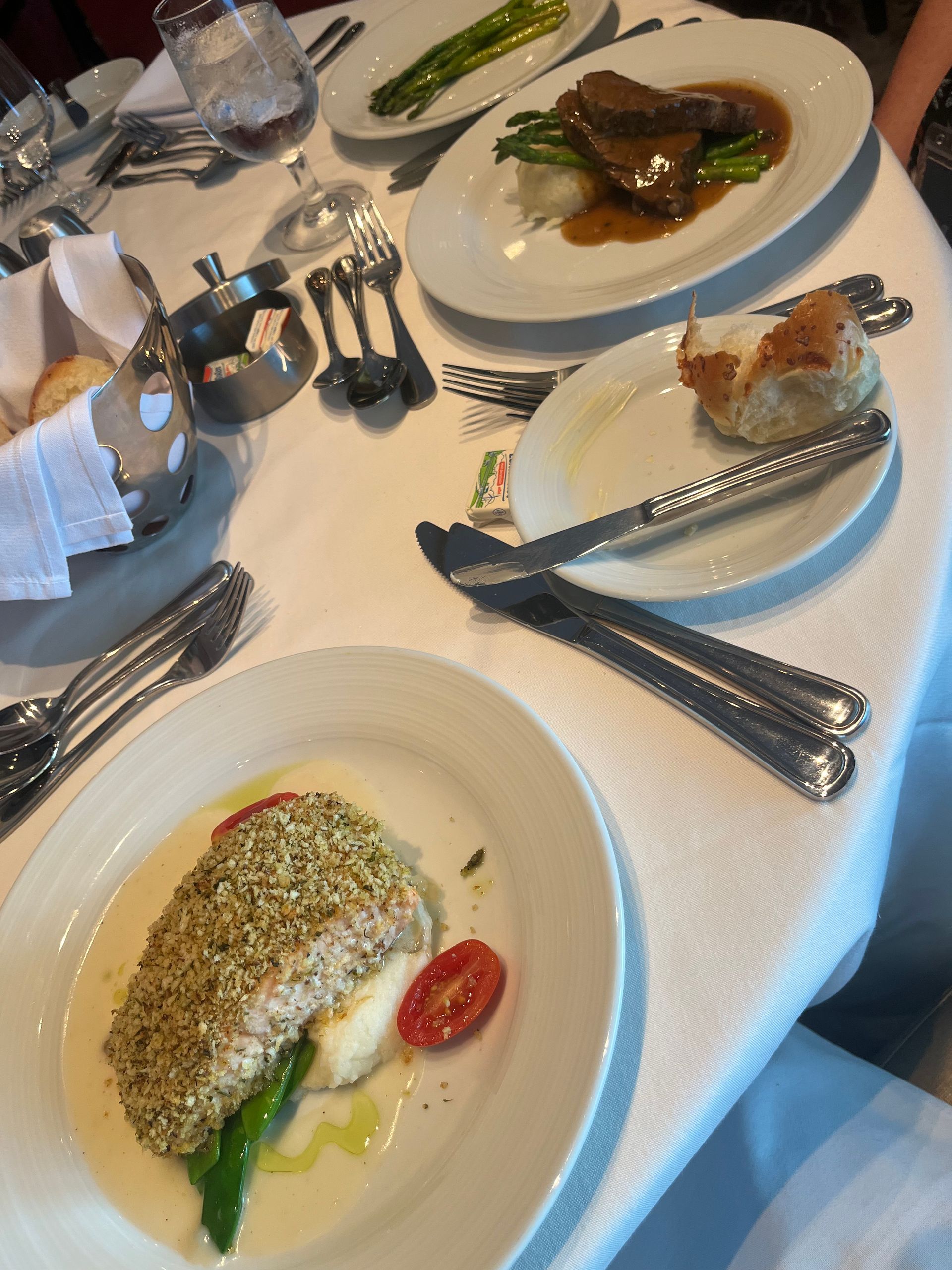 Elegant table set with plates of food: fish, meat, asparagus, bread rolls, and silverware.