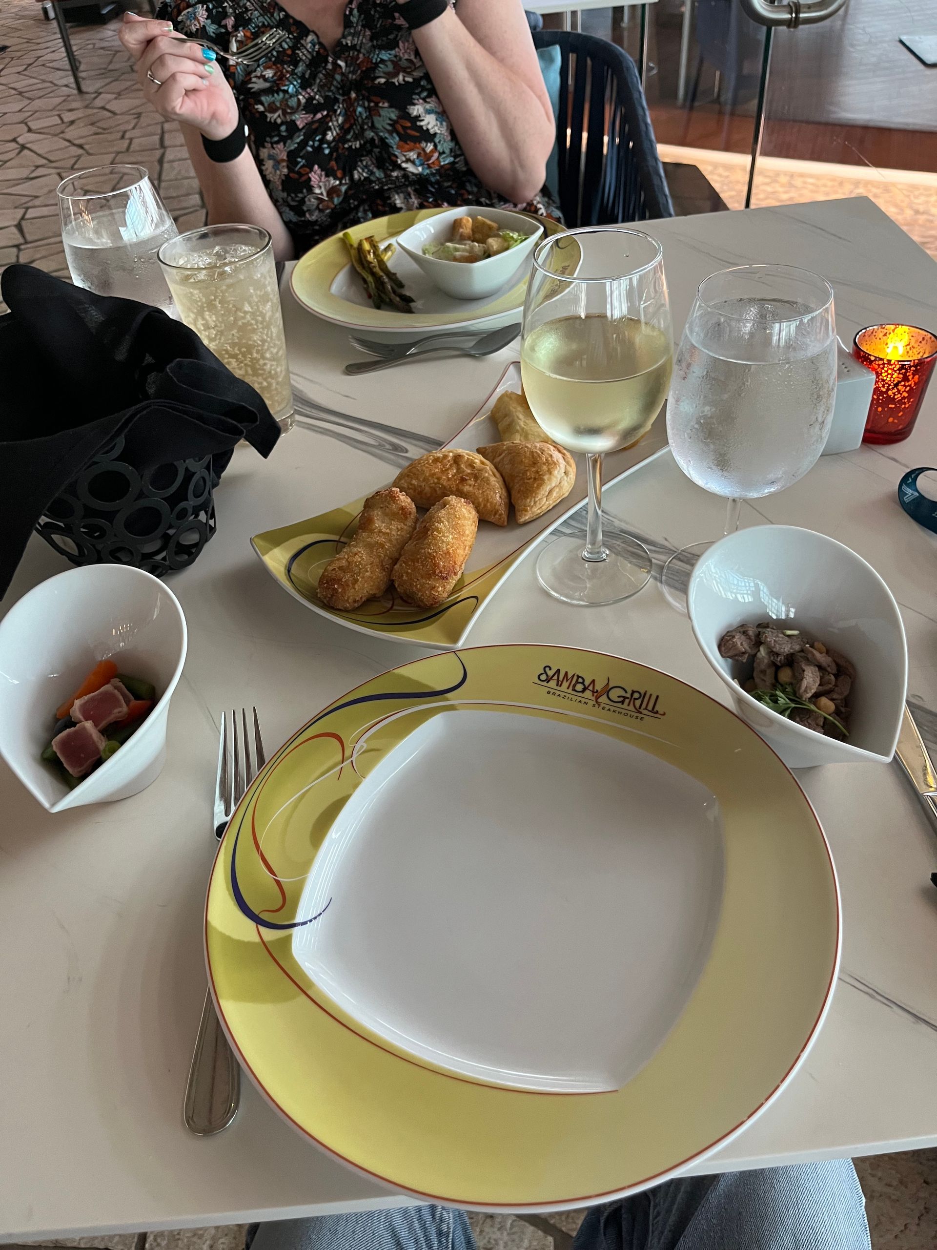 Table setting with food, drinks, and a person. Yellow plates, glasses, and appetizers are visible.
