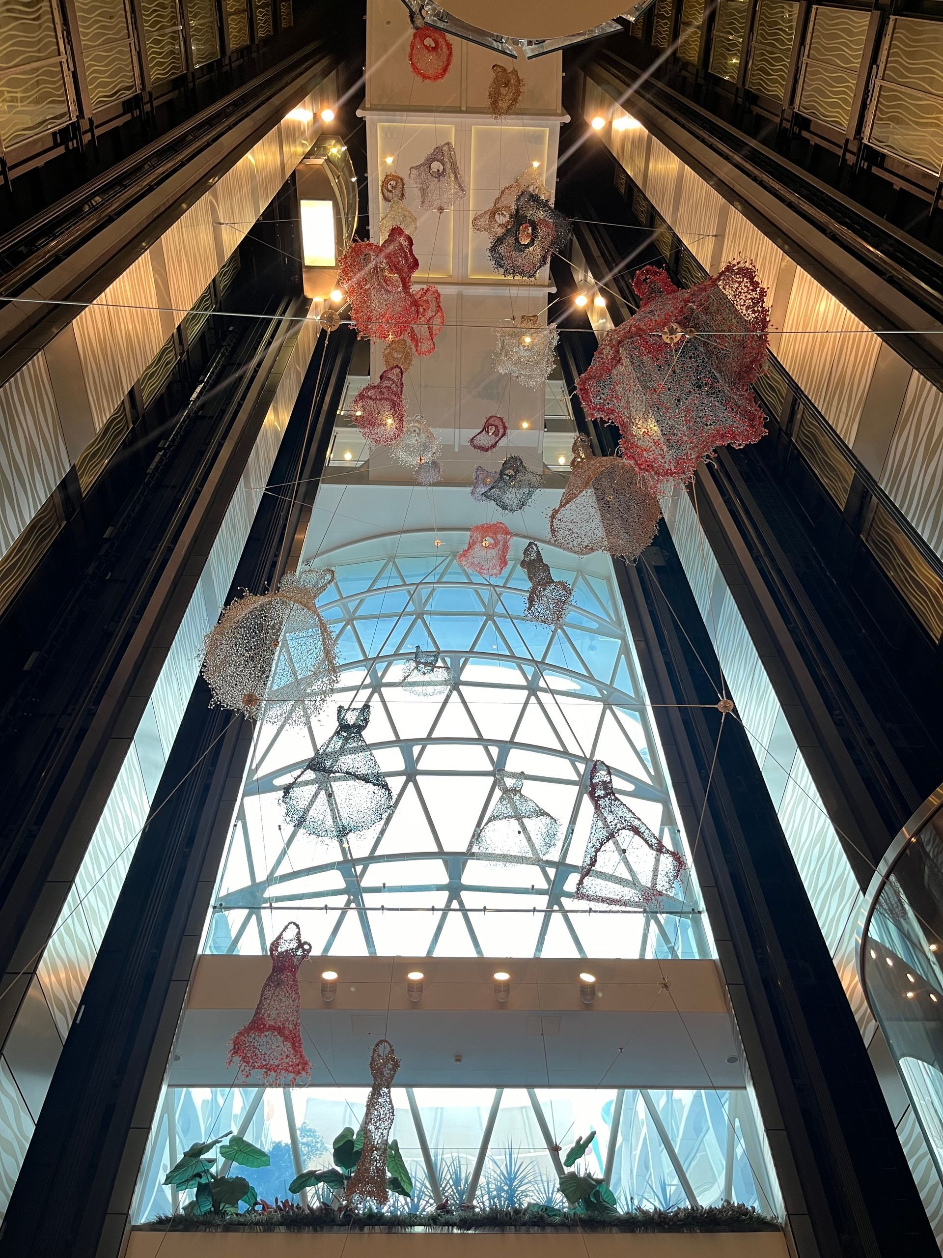 A tall atrium with elevators, decorative sculptures, and a geometric window looking toward the sky.