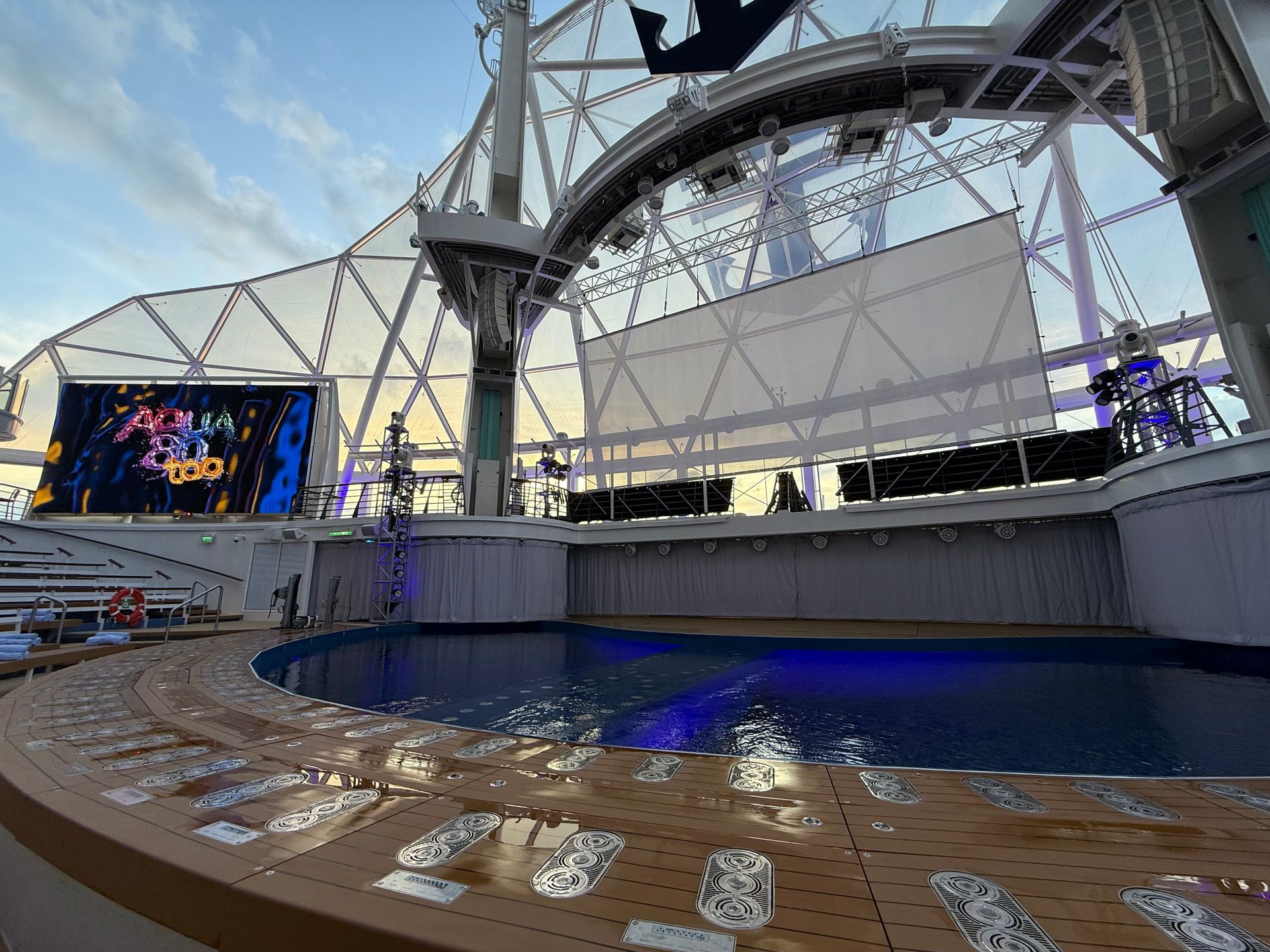 Pool deck with stage setup, large screen, and domed ceiling on a cruise ship.