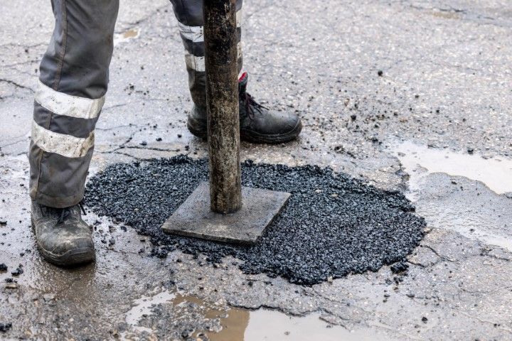Person with gray pants and reflective strips stamping asphalt into a pothole to repair area
