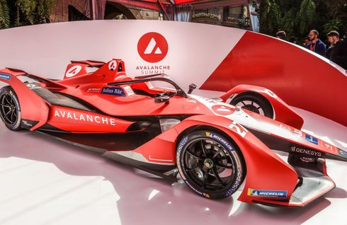 A bright red Avalanche Andretti Formula E race car sits on display in front of a matching branded backdrop.