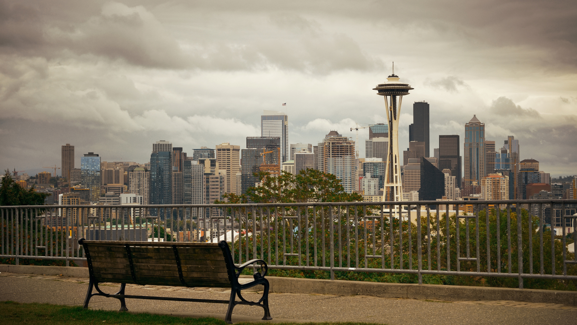 Seattle skyline view with Space Needle and a park bench under an overcast sky.