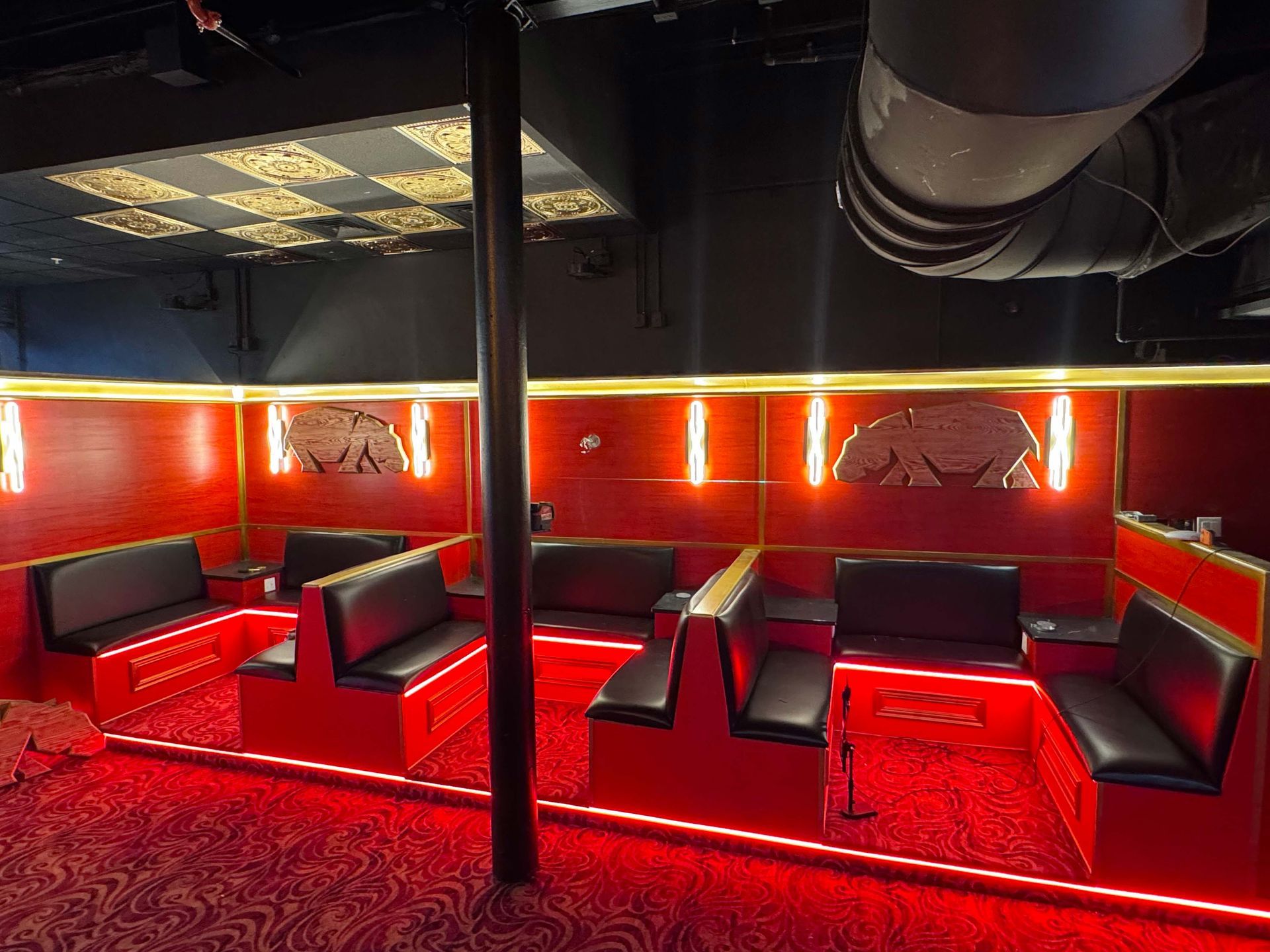 A lounge area with red walls, red carpet, and black upholstered booths arranged in a U-shape under warm, ambient lighting.